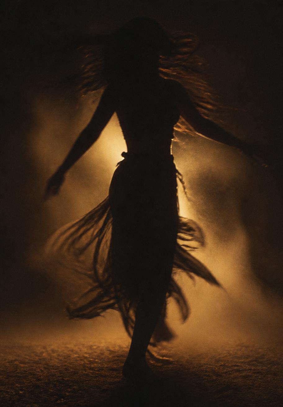 Silhouette of a dancer turning in warm dust and darkness