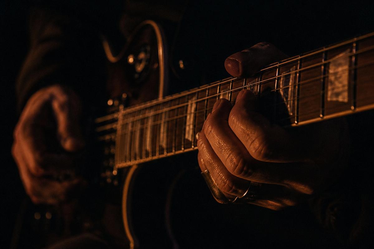 Hands on a guitar neck lit by low firelight