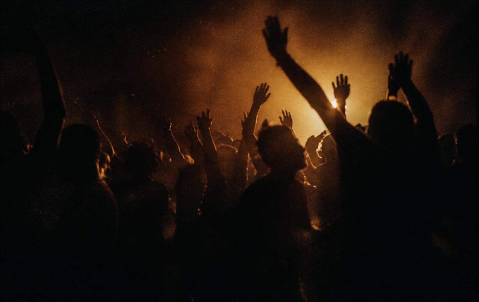 Backlit silhouettes of a crowd dancing in dust and warm haze