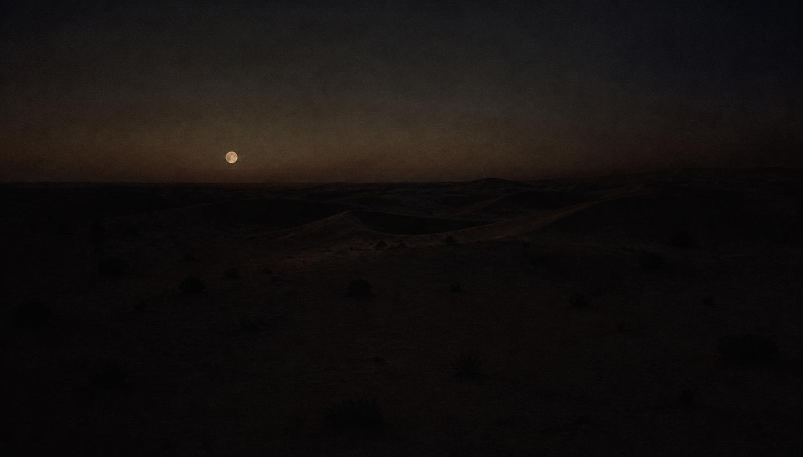 A moon low over dark desert dunes at night